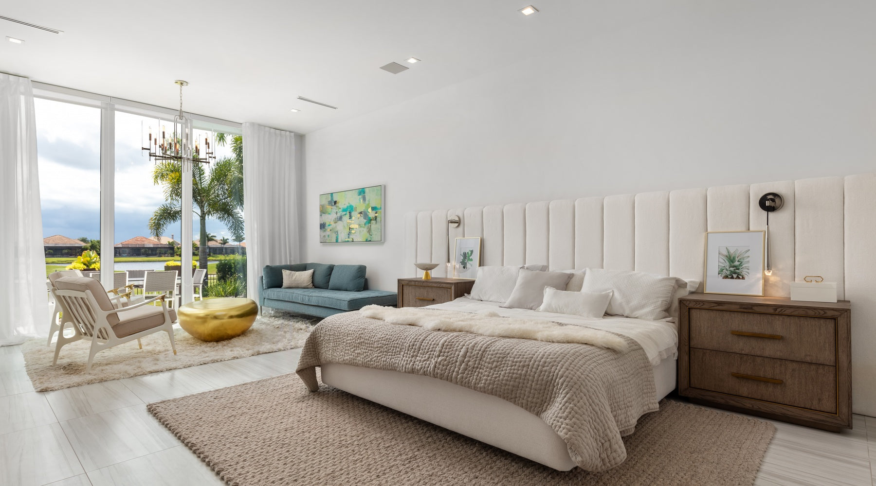 A modern bedroom with a king-size bed, a large bedframe, a rug, wooden nightstands, a sitting area and tall windows.