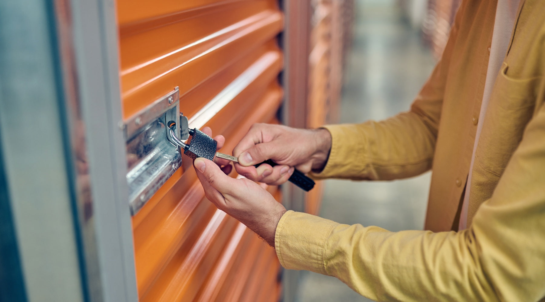 A man using a key to lock a padlock that is attached to the exterior of an orange storage unit door.