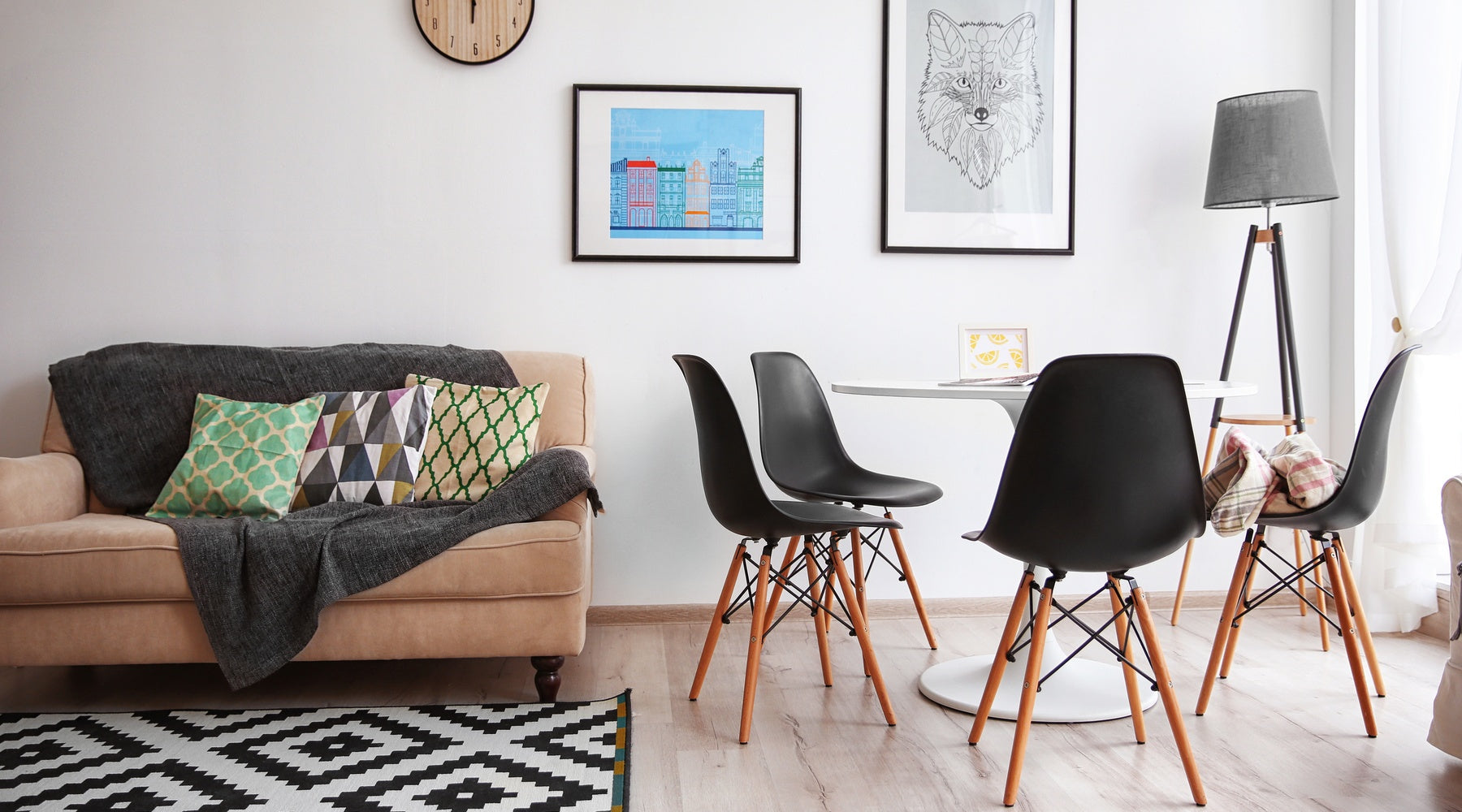 A home's living room features a small sofa, two framed pieces of art, a small table, and a black-and-white rug.