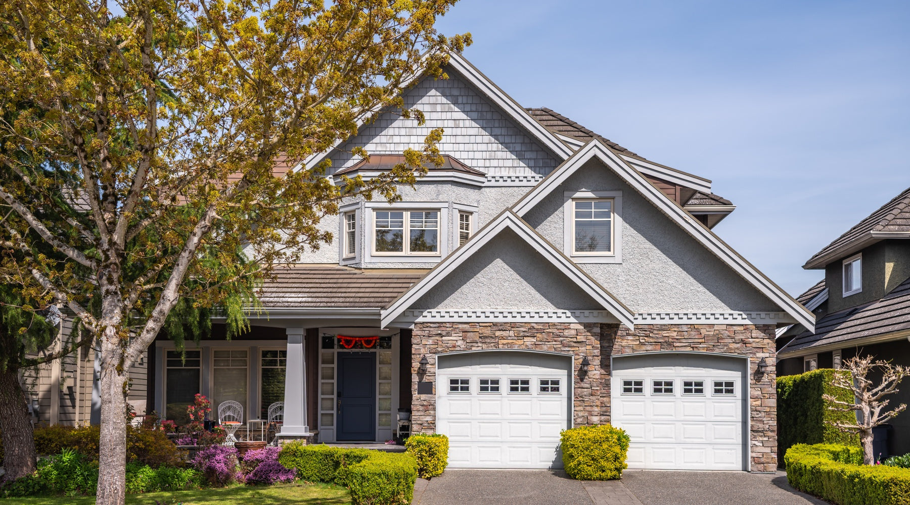 A two-story house with a blossoming tree in the front yard. The house has a two-car garage and a small porch.