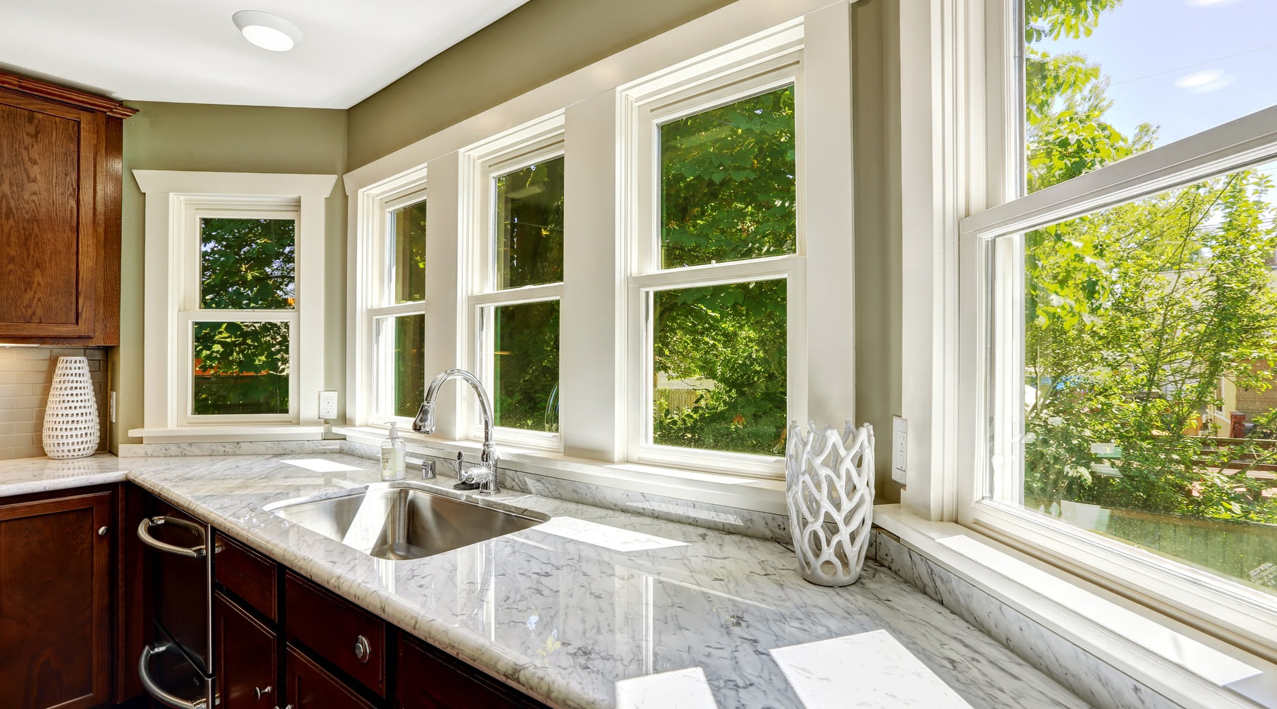 A kitchen with windows along the wall behind the sink. The windows are clean and reveal a sunny yard.