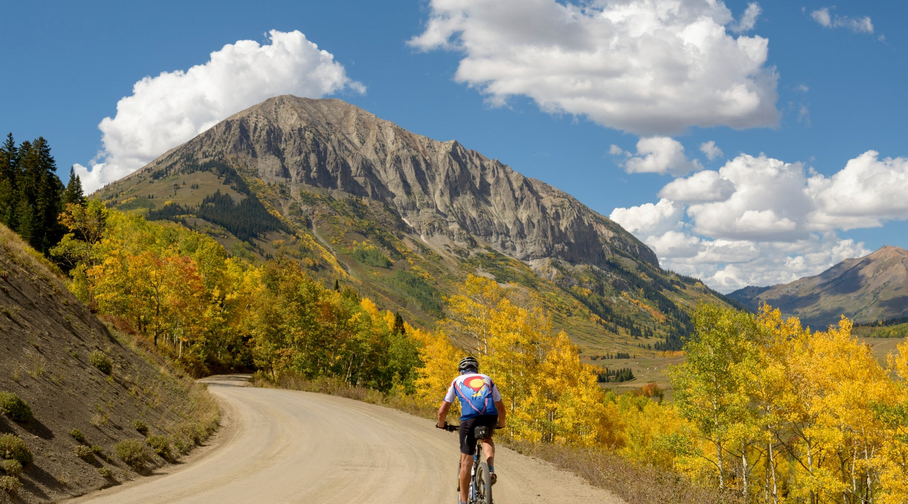 A man on a mountain bike rides toward Gothic Mountain in Crested Butte, Colorado in the fall.