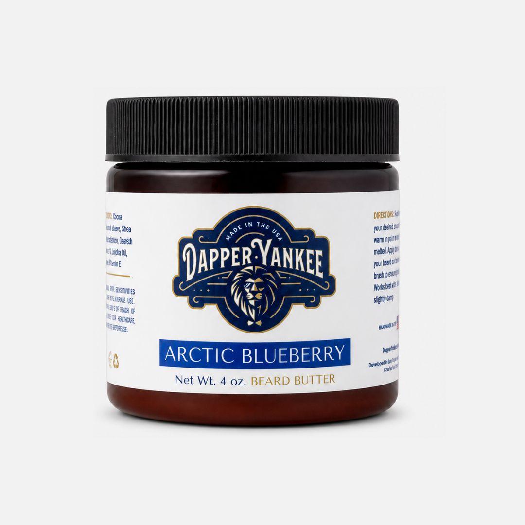 A 4 oz jar of Dapper Yankee Arctic Blueberry Beard Butter on a light gray background. The jar has a dark amber-brown body, a black ribbed screw cap, and a white label featuring the brand's blue and black logo and the product name 'Arctic Blueberry'.