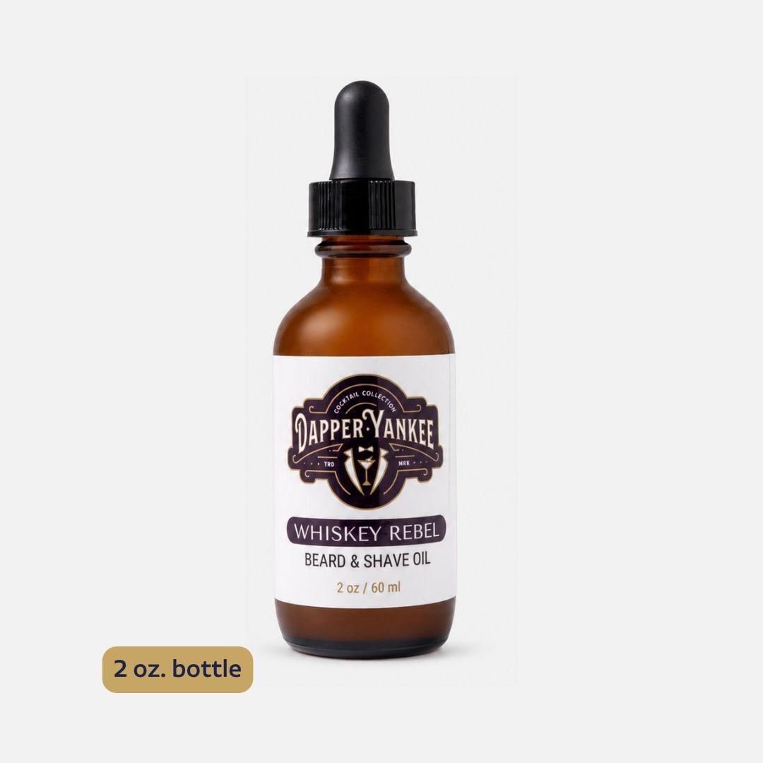 An amber glass dropper bottle of Dapper Yankee Whiskey Rebel Beard & Shave Oil on a light gray background, with a brown '2 oz. bottle' label overlay in the bottom left corner.