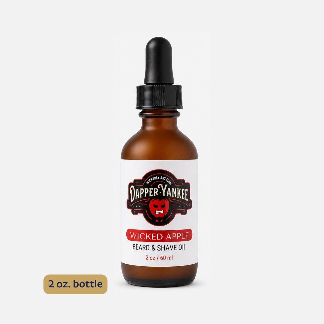 An amber glass dropper bottle of Dapper Yankee Wicked Apple Beard & Shave Oil on a light gray background, with a small '2 oz. bottle' label overlay in the bottom left corner.